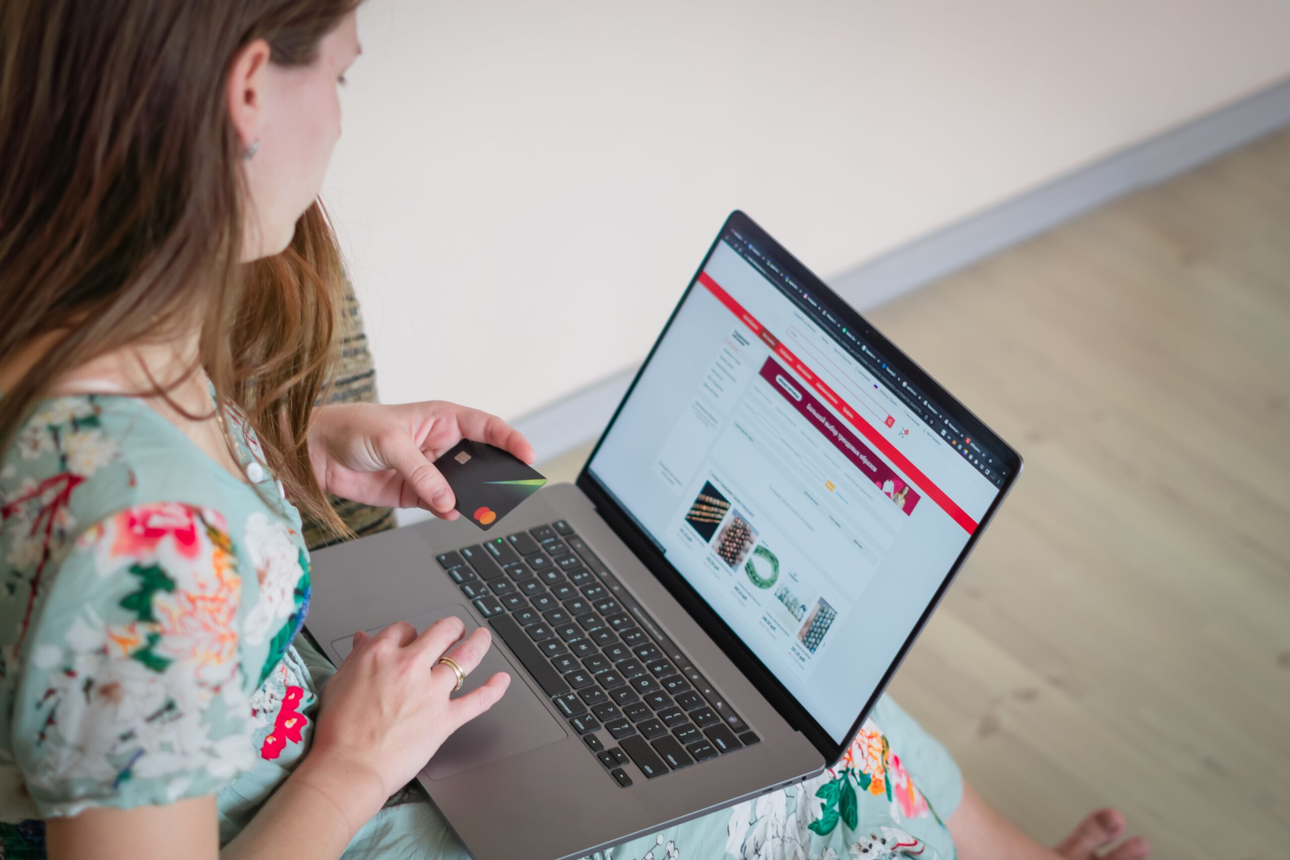 Web Designing & Development Woman in floral dress shopping online with a laptop and credit card indoors.